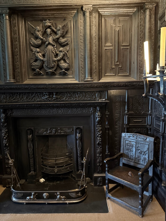 Dark wood-panelled room at Malahide Castle featuring an intricately carved fireplace with angels and figures above, and a wooden chair to the side.