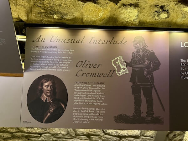 Exhibit panel titled “An Unusual Interlude” focuses on Oliver Cromwell with a painted portrait, stylized illustration, and text describing his role at the castle, displayed on a muted gray and gold background.