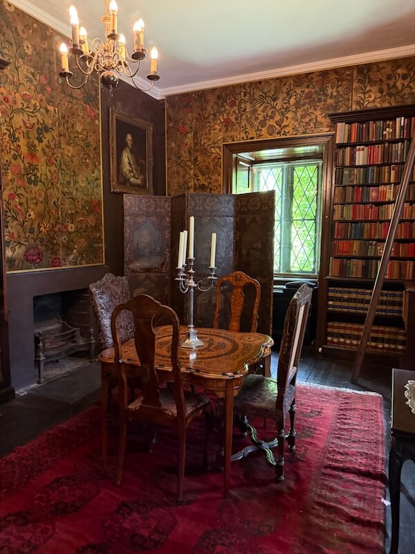 Historic room inside Malahide Castle, Dublin, featuring a wooden table with carved chairs, candelabra, bookshelves, chandelier, and patterned wallpaper with floral designs.