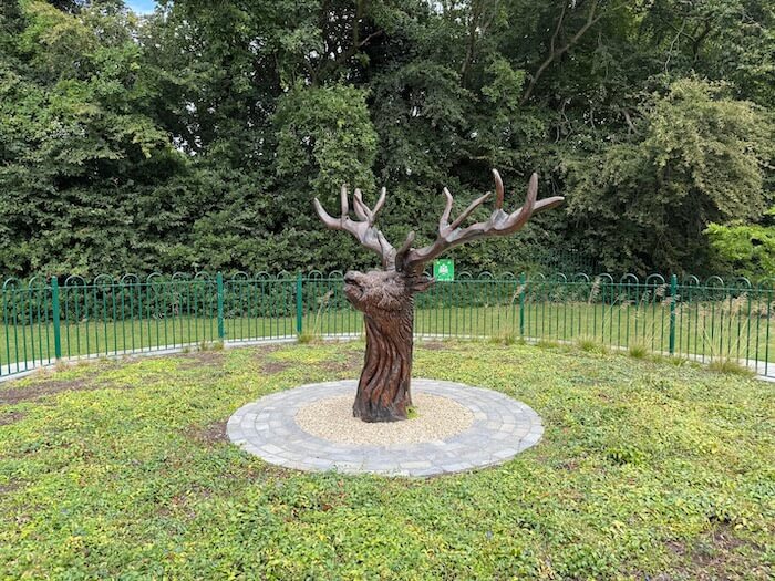 Wooden sculpture of a stag’s head carved from an old tree trunk in the gardens of Malahide Castle, Dublin, set against a backdrop of greenery.