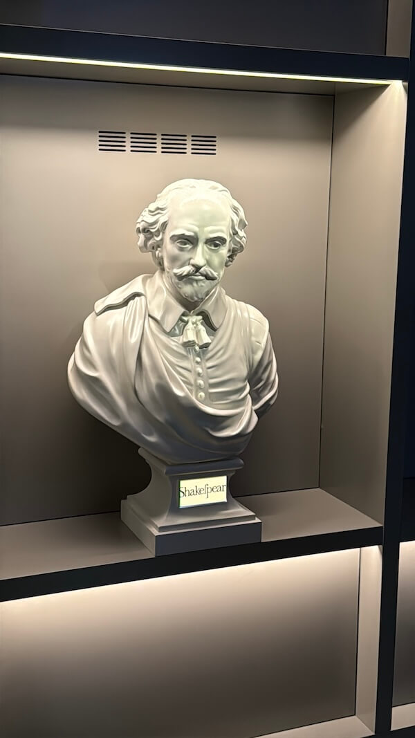 White bust of William Shakespeare displayed in a modern, softly lit niche, labelled with his name at the base in a stylised serif font.