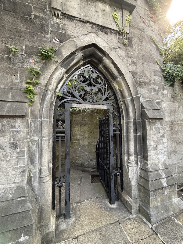Stone Gothic-style arched doorway with iron gate leading to Marsh's Library, surrounded by ivy and engraved with a Latin inscription above the entrance.