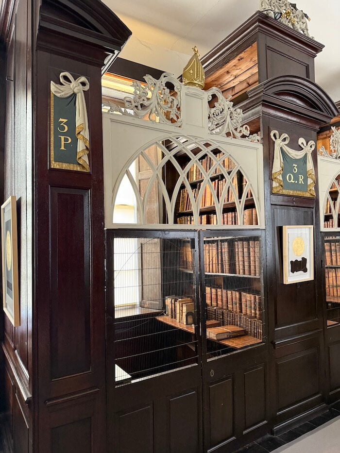 Ornate wooden reading cage inside Marsh’s Library with arched lattice trim and a golden bishop’s mitre on top, housing shelves of rare books behind metal bars.