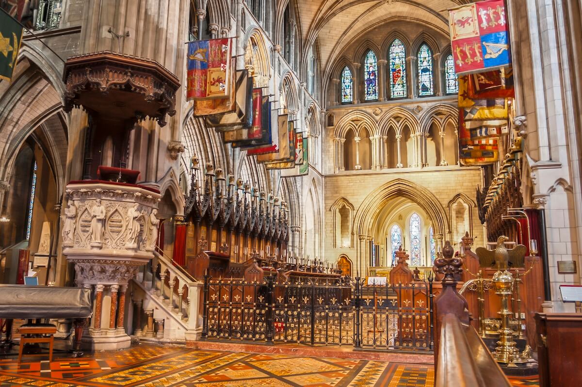 Interior of St. Patrick’s Cathedral in Dublin, showcasing ornate Gothic architecture, colorful stained glass windows, a carved stone pulpit, and rows of medieval heraldic banners hanging above the choir stalls.