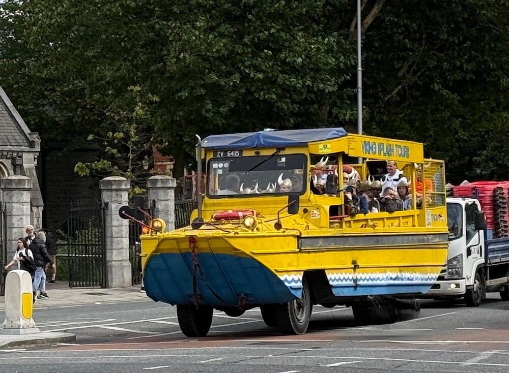 Bright yellow amphibious vehicle used for the Viking Splash Tours in Dublin, carrying passengers wearing Viking helmets as it drives through the city streets. The front of the vehicle is painted blue.