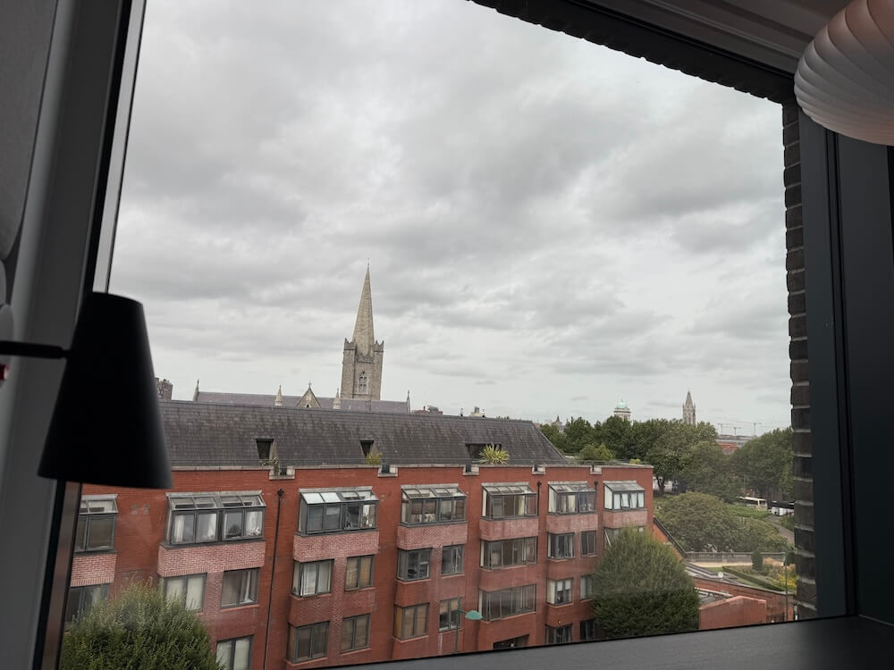 View through a window on a grey, overcast day showing red-brick apartment buildings and the pointed spire of a Gothic-style church in the background. 